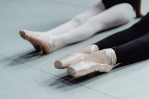 crop female ballet dancers sitting on floor in studio