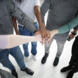 crop multiracial people joining hands together during break in modern workplace